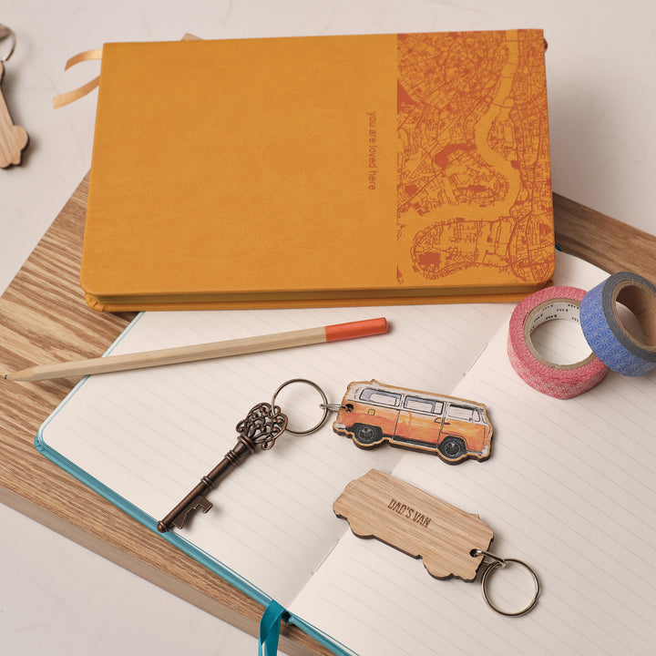Wooden keychain keyring shaped like an orange VW campervan on an open book with stationery items. Personalised text on the back saying 'Dad's Van'. Perfect gifts for him.
