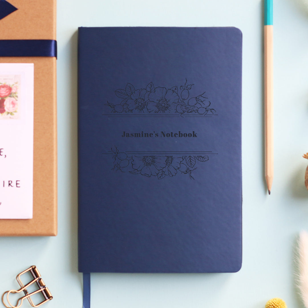 A beautifully designed floral navy blue notebook featuring a custom name, ideal for personal notes and creative writing, Charming florals with a unique personalization, inviting creativity and inspiration on every page.