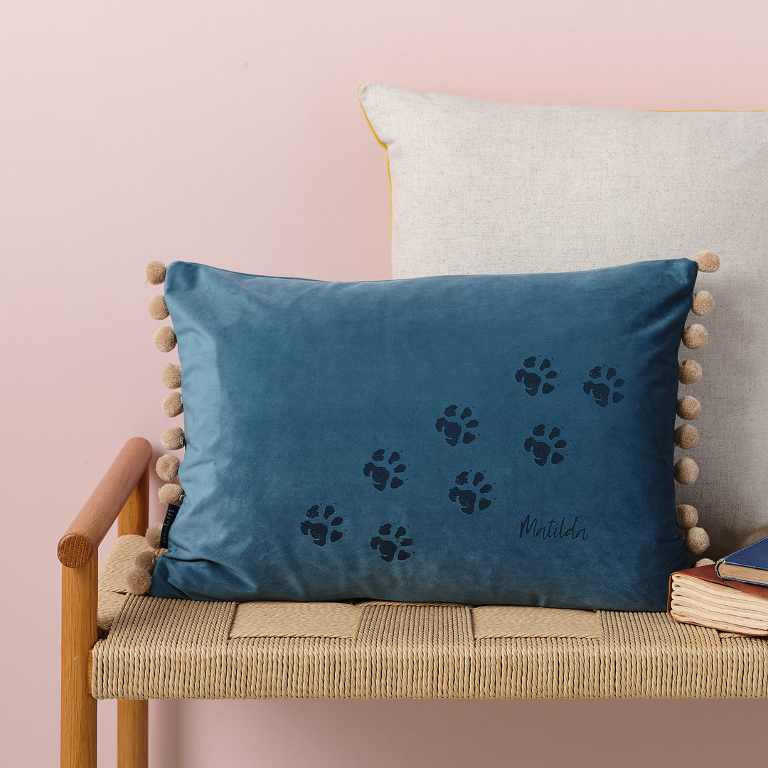 A blue velvet cushion with paw prints and the name Matilda embroidered on it.
