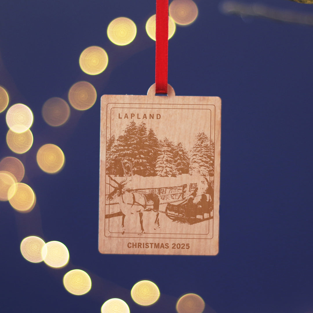 Lapland travel memory anniversary gift, commemorate your Christmas memories, with this sustainable wood cherry veneered ornament with Father Christmas and his reindeer. Hanging against a blue background. Personalise the location and text for a perfect letterbox friendly gift for travellers.