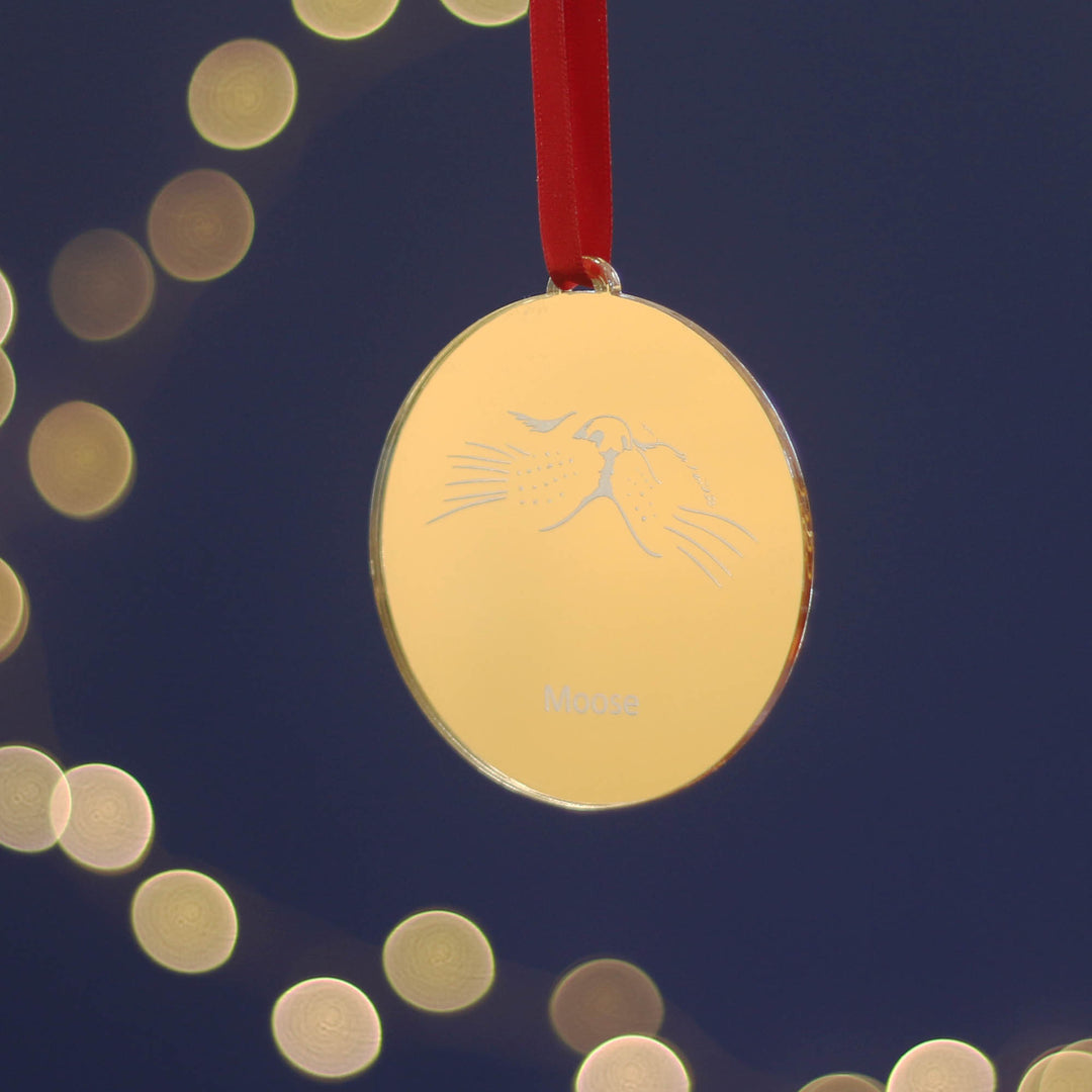 Golden mirrored luxury Christmas tree decoration with a cat design personalised with your pets name on a dark blue background with blurred lights and hung with red ribbon. Designed as a bespoke gift for cat lovers.