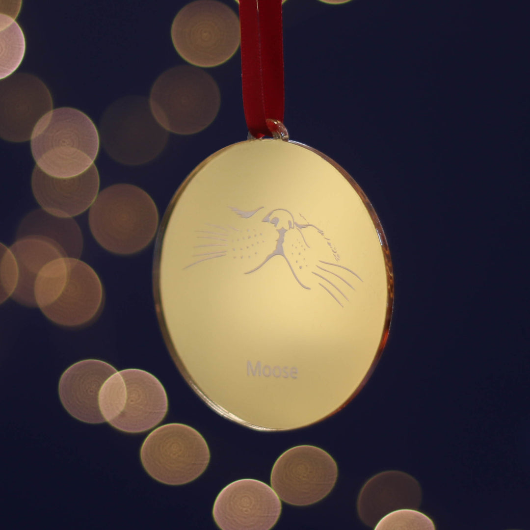 Golden Christmas tree decoration with an adorable pet cat nose emblem on a dark background with blurred lights strung with a red satin ribbon. Add some magical Christmas sparkle to your tree, or gift it to a cat loving friend!