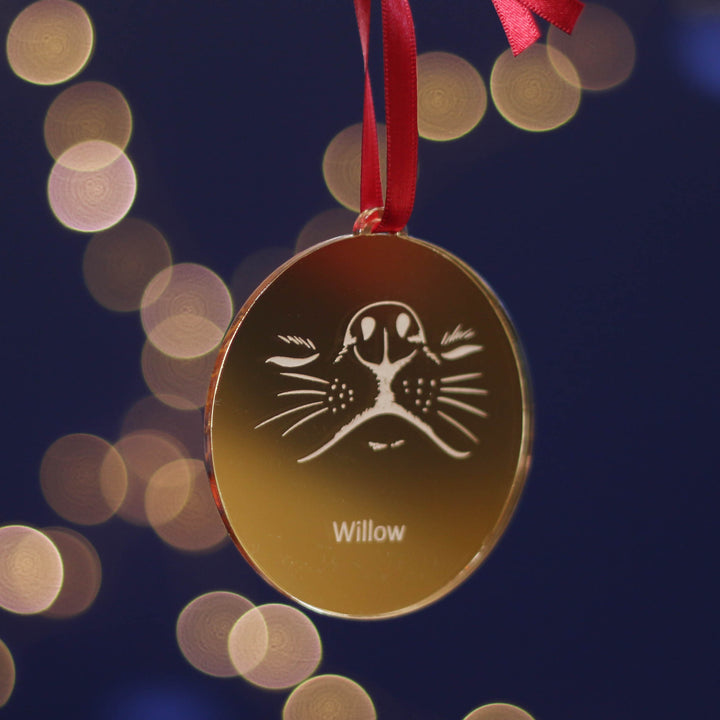 Gold Christmas tree ornament with a dog design and personalised pet name, hanging against a blurred light background. Perfect Christmas gift for dog lovers.