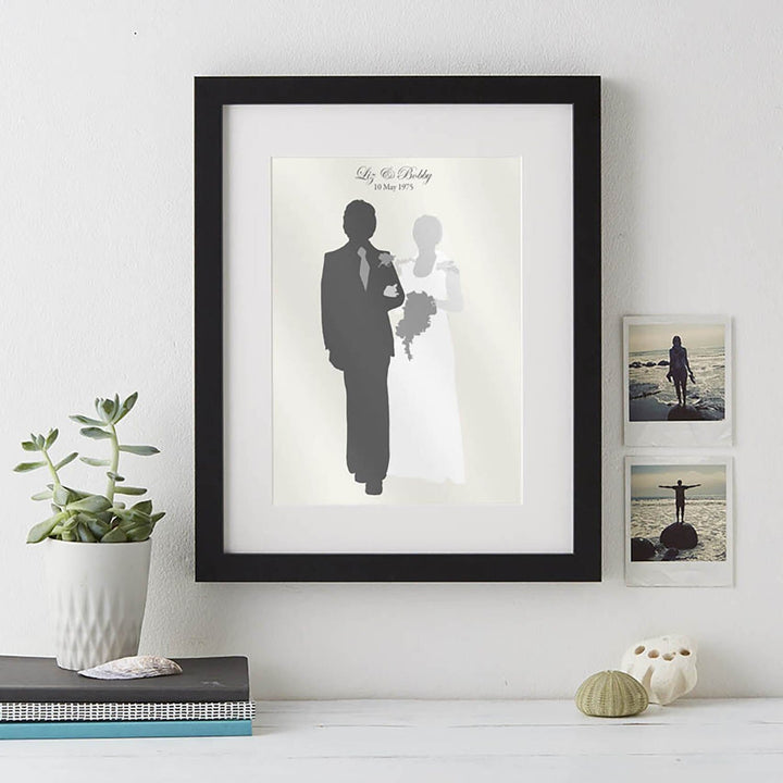 A wedding silhouette portrait in a black frame. The bride and groom are walking hand in hand on a white background. Their names and wedding date are written at the top.