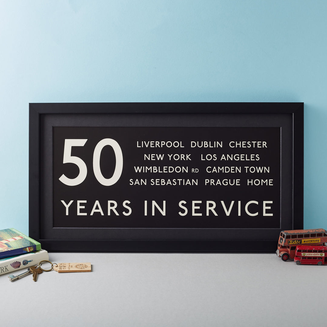 a framed black and white print in the style of a routemaster bus blind. Personalised with the line 50 years in service, and favourite destinations.