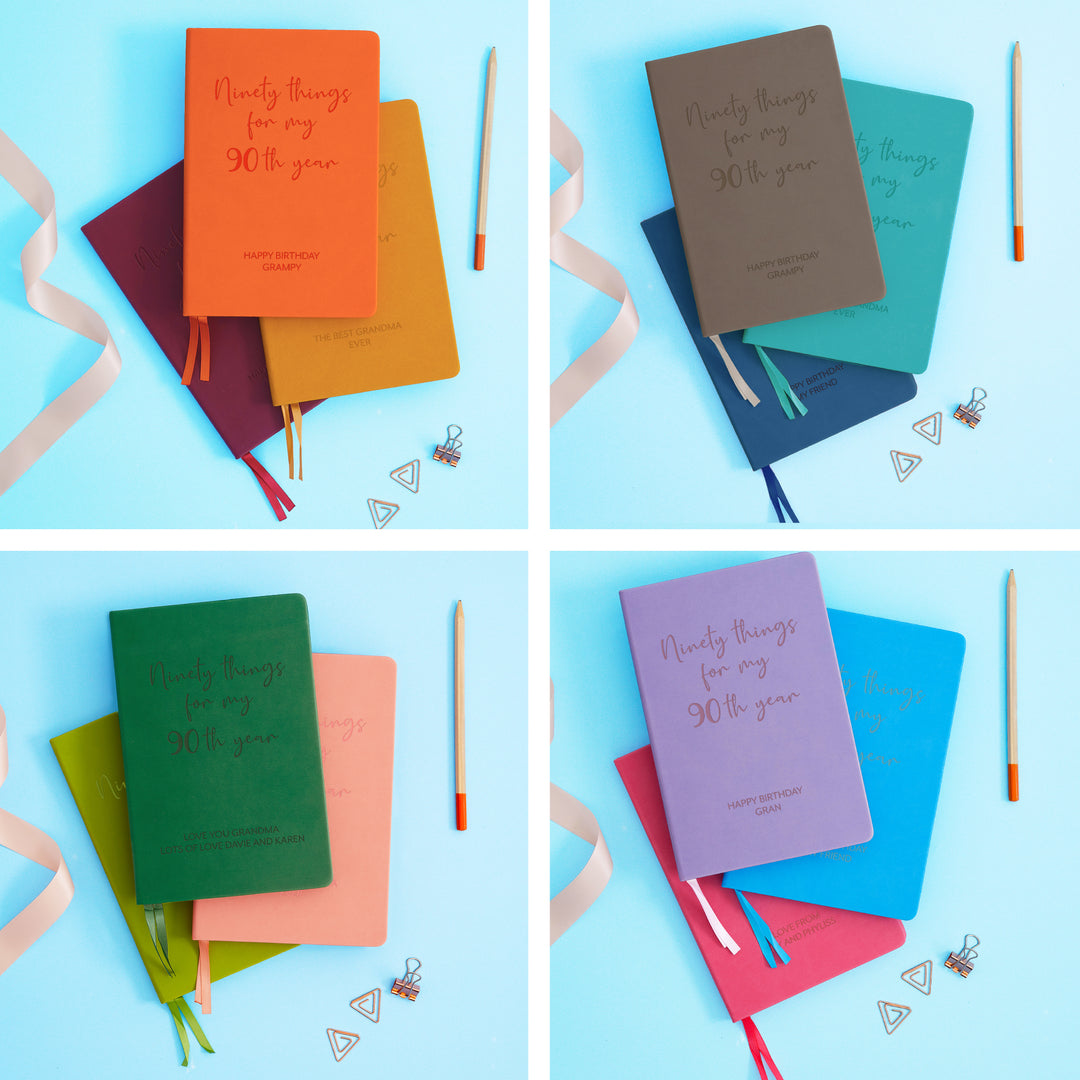 The image shows examples of personalised engraved text on all 12 colours of notebook. The books are stacked  in threes and are surrounded by various pieces of stationery.