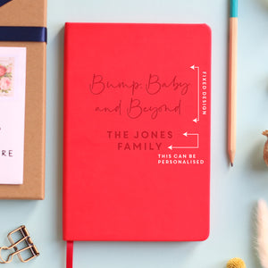 A top down image of a red vegan leather notebook resting on a pale aqua table. The front of the notebook features the phrase Bump, Baby and Beyond. The personalised engraving reads The Jones Family. Surrounding the book are various stationary items and dried flowers. the image is edited to show the text that can be personalised.