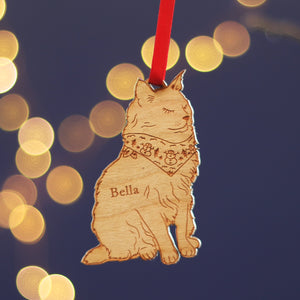 Cat pet wooden Christmas tree ornament with space for a custom name e.g. 'Bella' on a dark blue background with blurred lights, could be a custom Christmas gift tag, or a long loved family bauble.