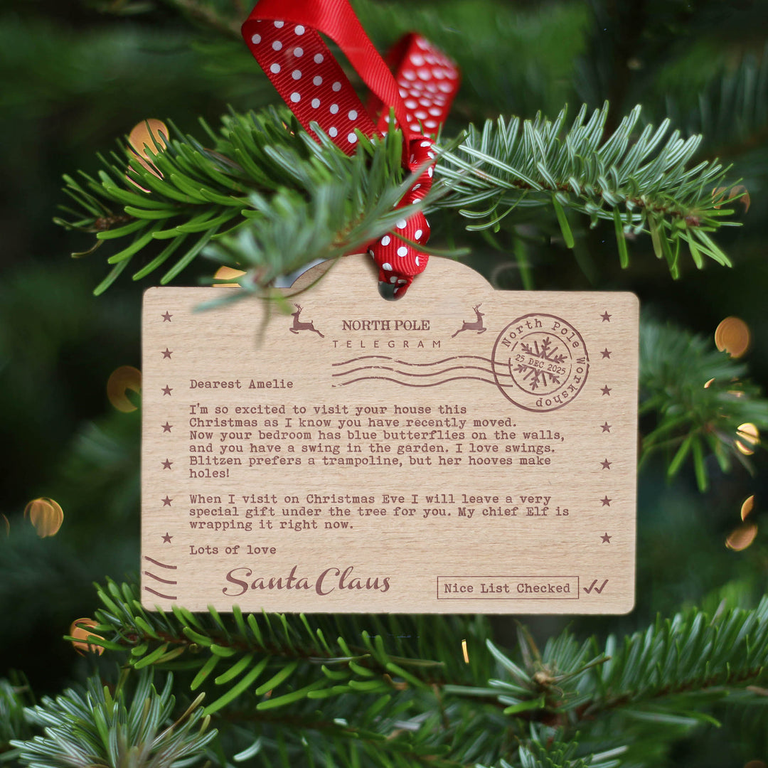 Santa's Nice list themed personalised wooden ornament with Santa Claus letter hung with red and white polka dot ribbon on a Christmas tree.