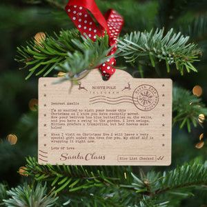Santa's Nice list themed personalised wooden ornament with Santa Claus letter hung with red and white polka dot ribbon on a Christmas tree.
