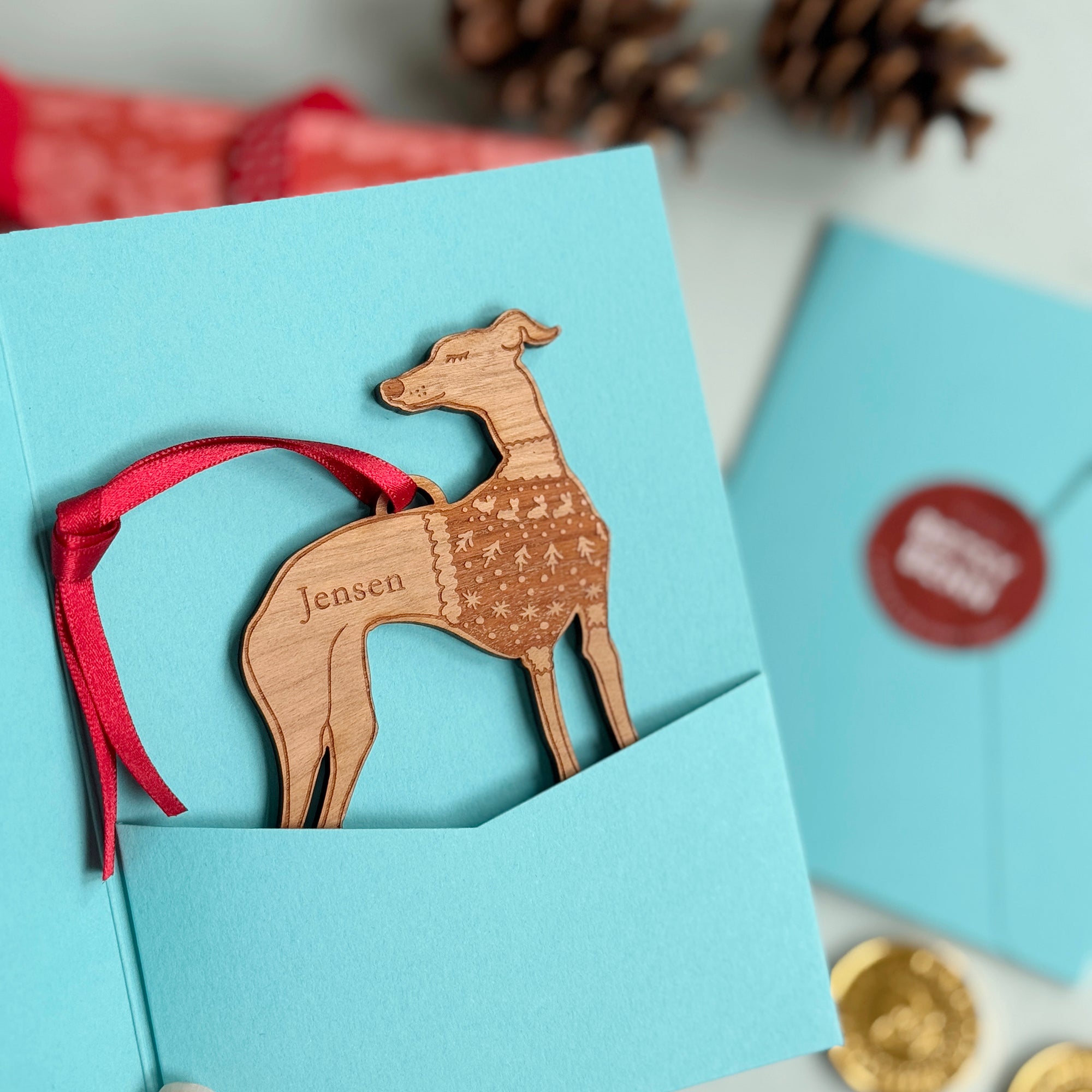 Wooden Whippet Christmas Tree bauble ornament in a blue gift card package, strung with a red ribbon. Gift for the Greyhound, Hound, Whippet, dog lover, in your life.