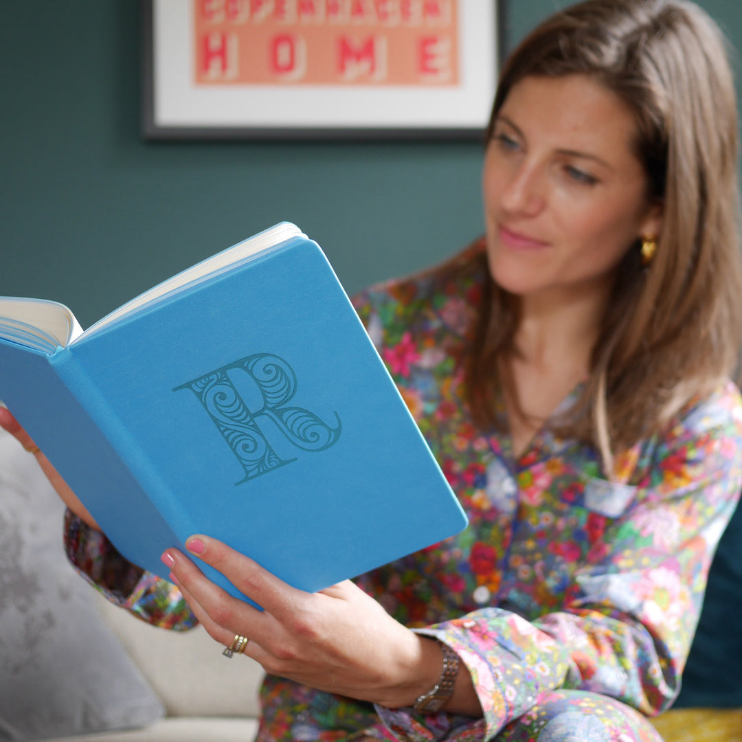 An image of women holding a blue vegan leather notebook. The front of the notebook is personalised with the letter R engraved in a large decorative font.