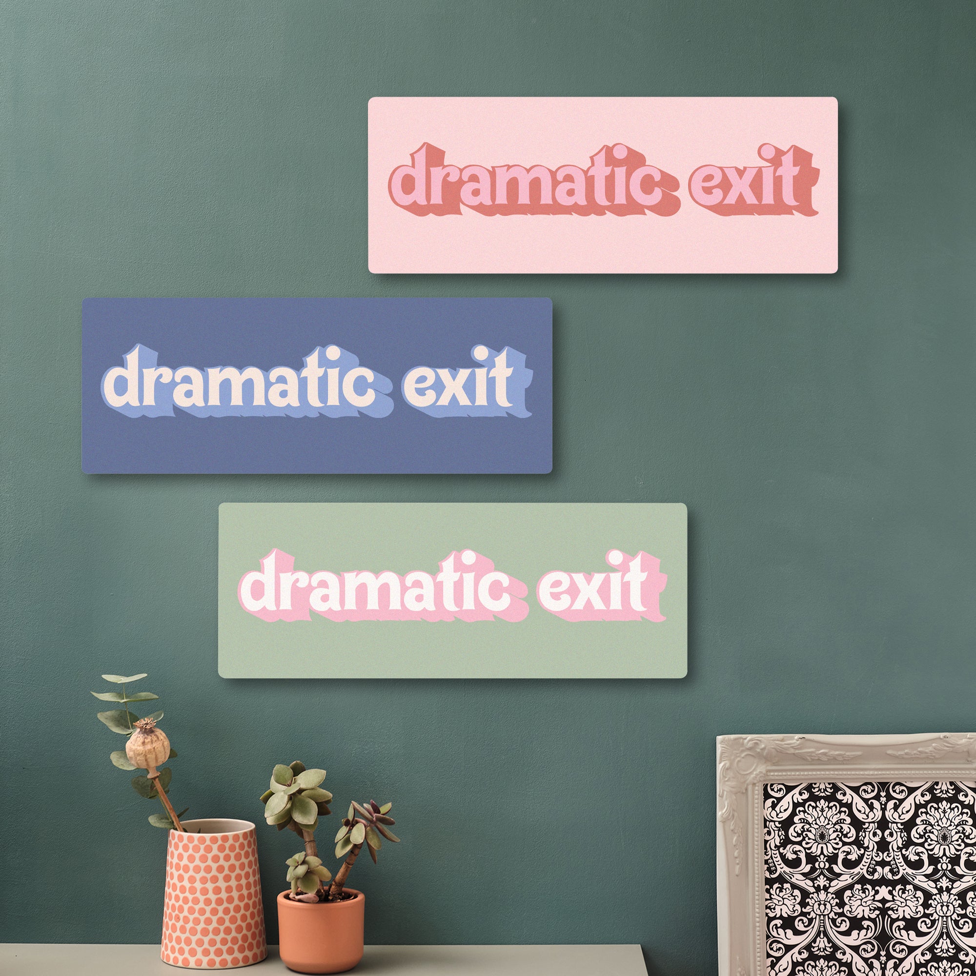 Close-up of a green wooden sign reading “dramatic exit” in playful retro lettering, mounted on a green wall surrounded by hexagon wall tiles and potted plants.