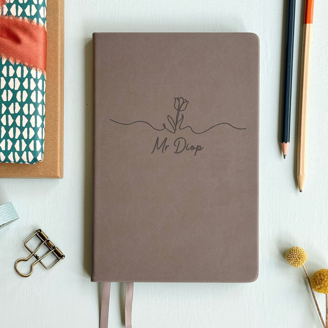 Floral motif tasteful end of year teacher gift grey notebook on pale grey background surrounded by stationery.