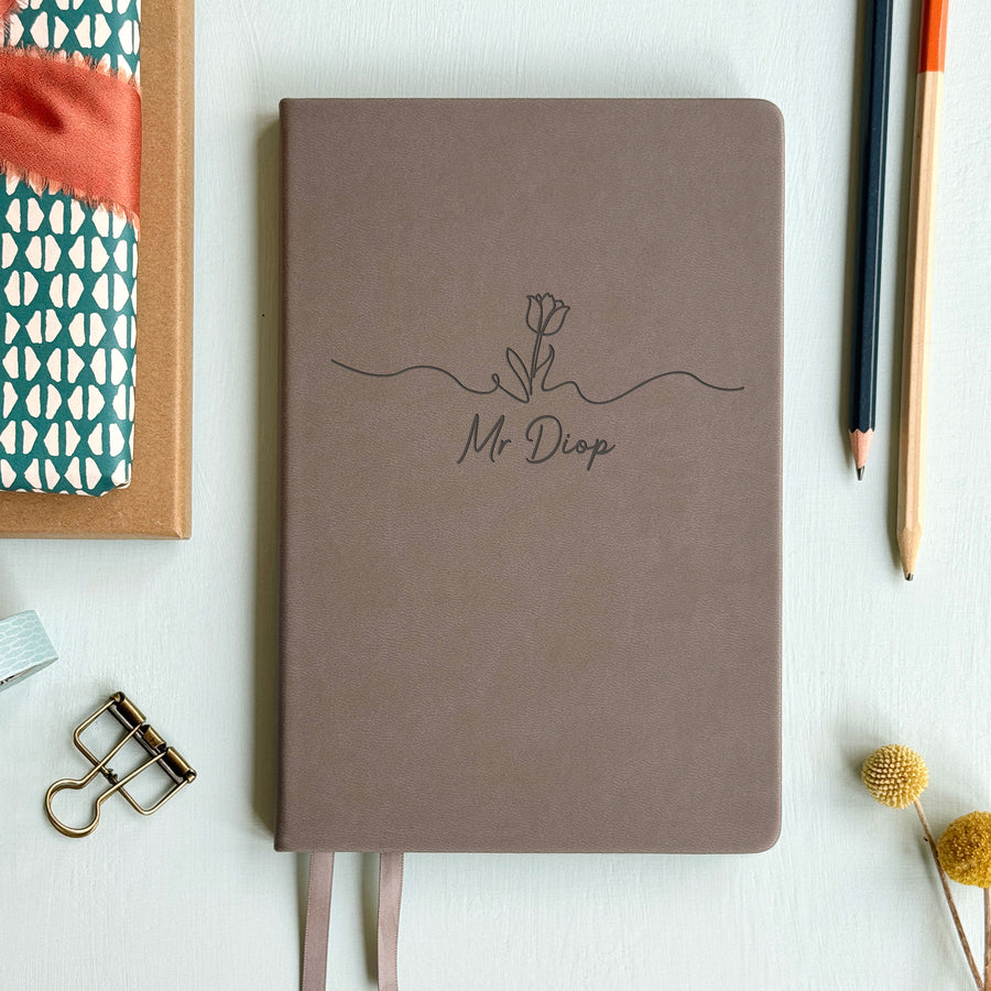 Floral motif tasteful end of year teacher gift grey notebook on pale grey background surrounded by stationery.