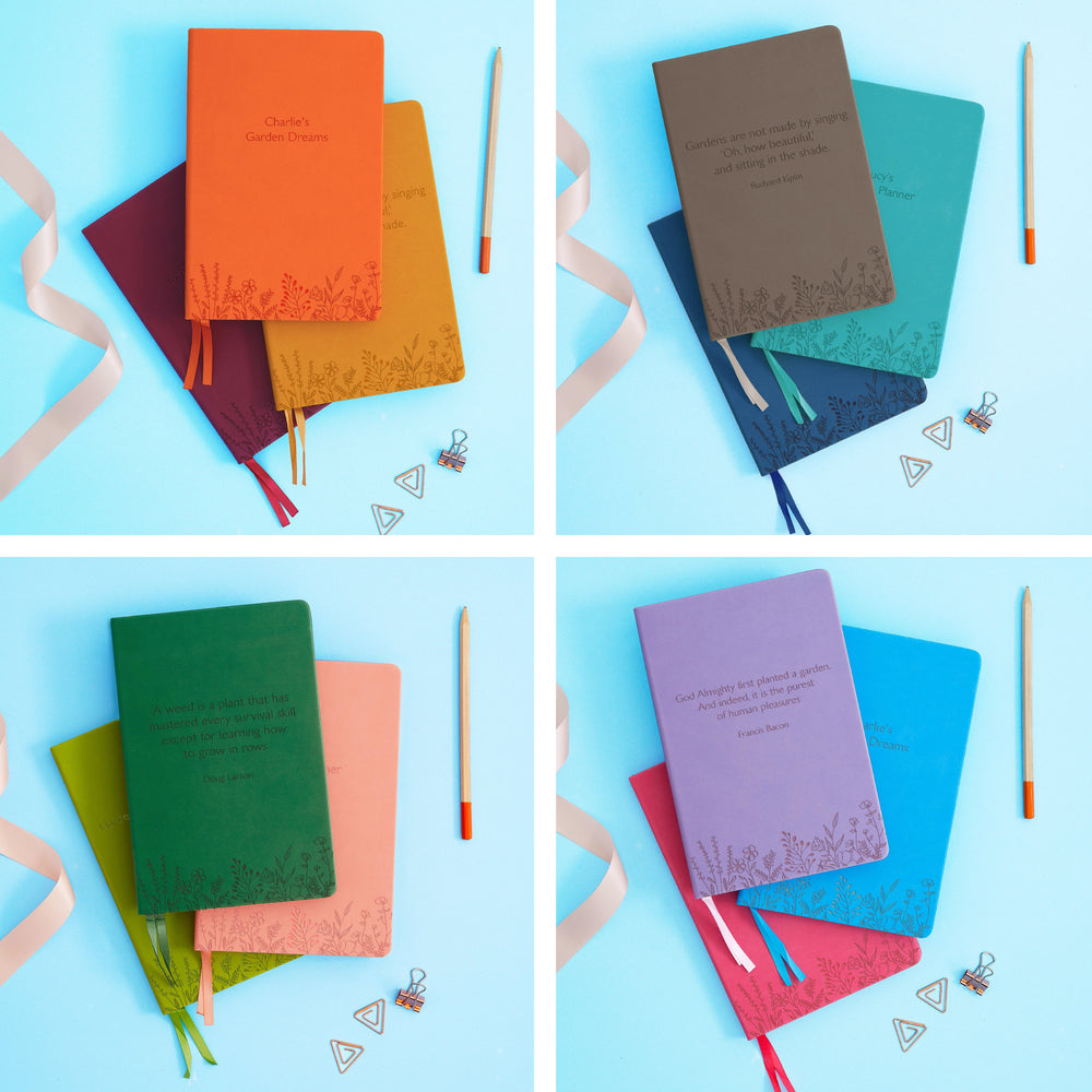 The image shows examples of personalised engraved text on all 12 colours of notebook. The books are stacked in threes and are surrounded by various pieces of stationery.