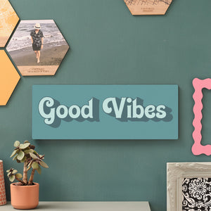 Quirky wooden quote sign reading Good Vibes, styled as bold hallway wall decor next to modern photo hexagons and leafy houseplants.