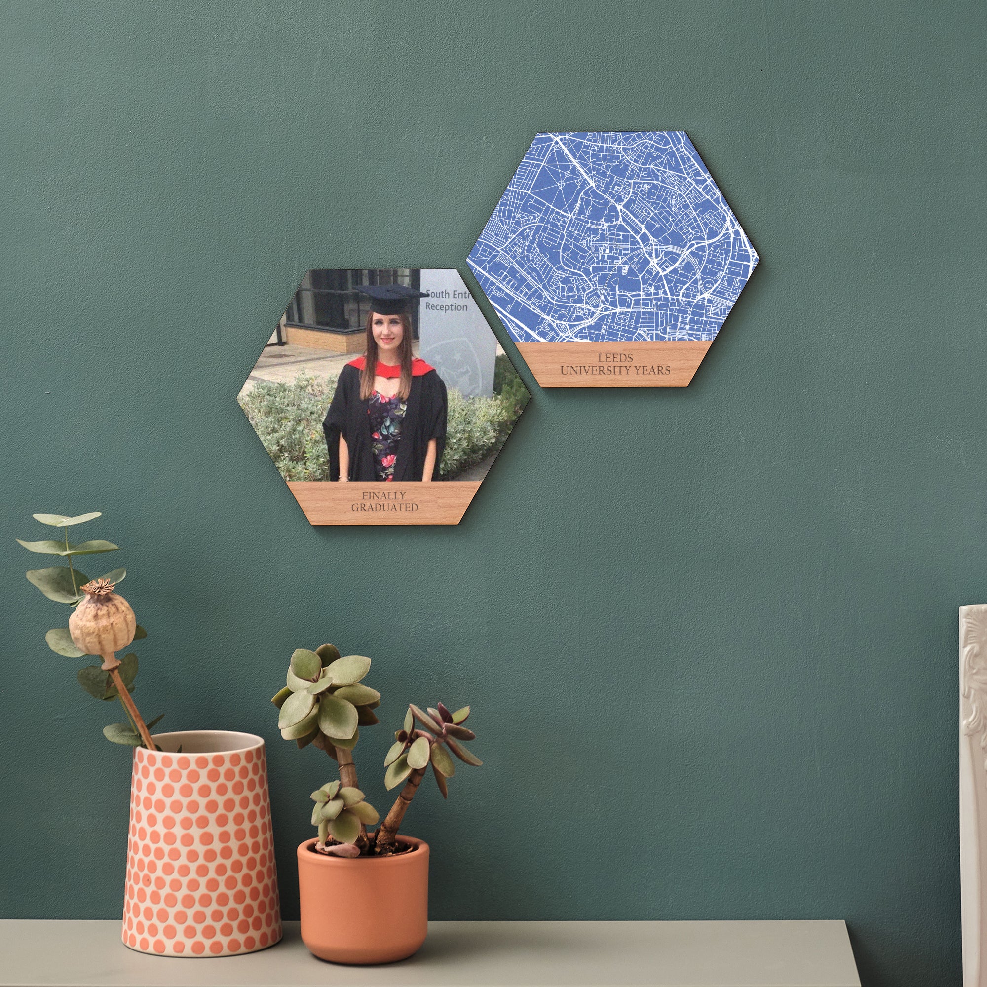 A heartfelt graduation present gift set of two hexagon wooden tiles. One shows a young woman in cap and gown. One shows a map of Leeds University. Displayed on a green wall.