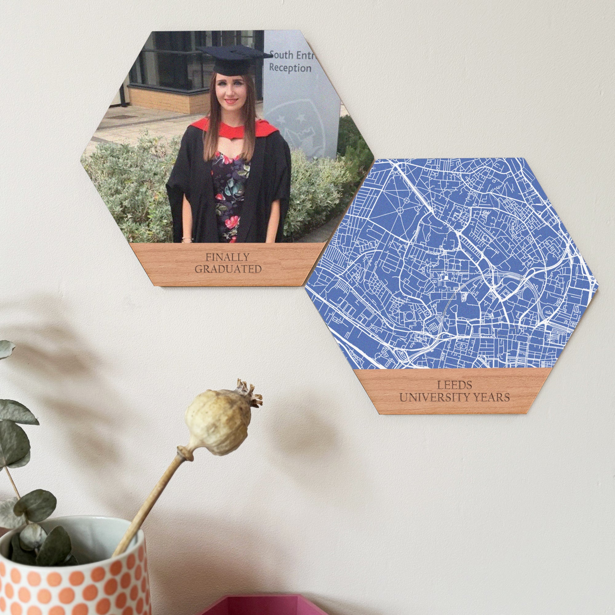 A graduation present gift set of two hexagon wooden tiles. One shows a young woman in cap and gown. One shows a map of Leeds University. Displayed on a pink wall.