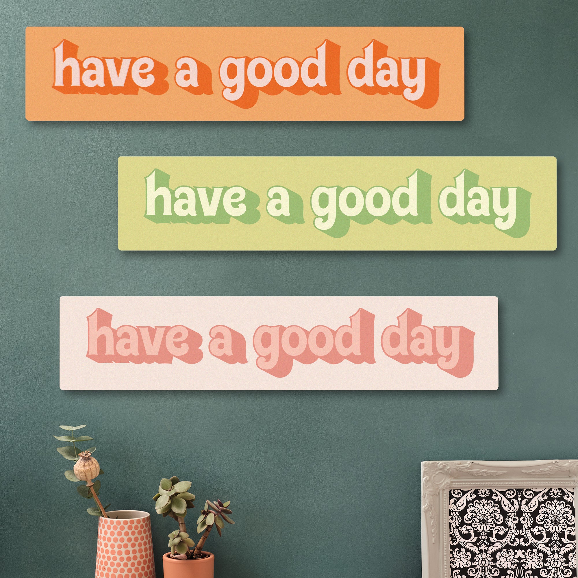 “Have a Good Day” in pinks wooden sign on green gallery wall with plants and photo hexagons