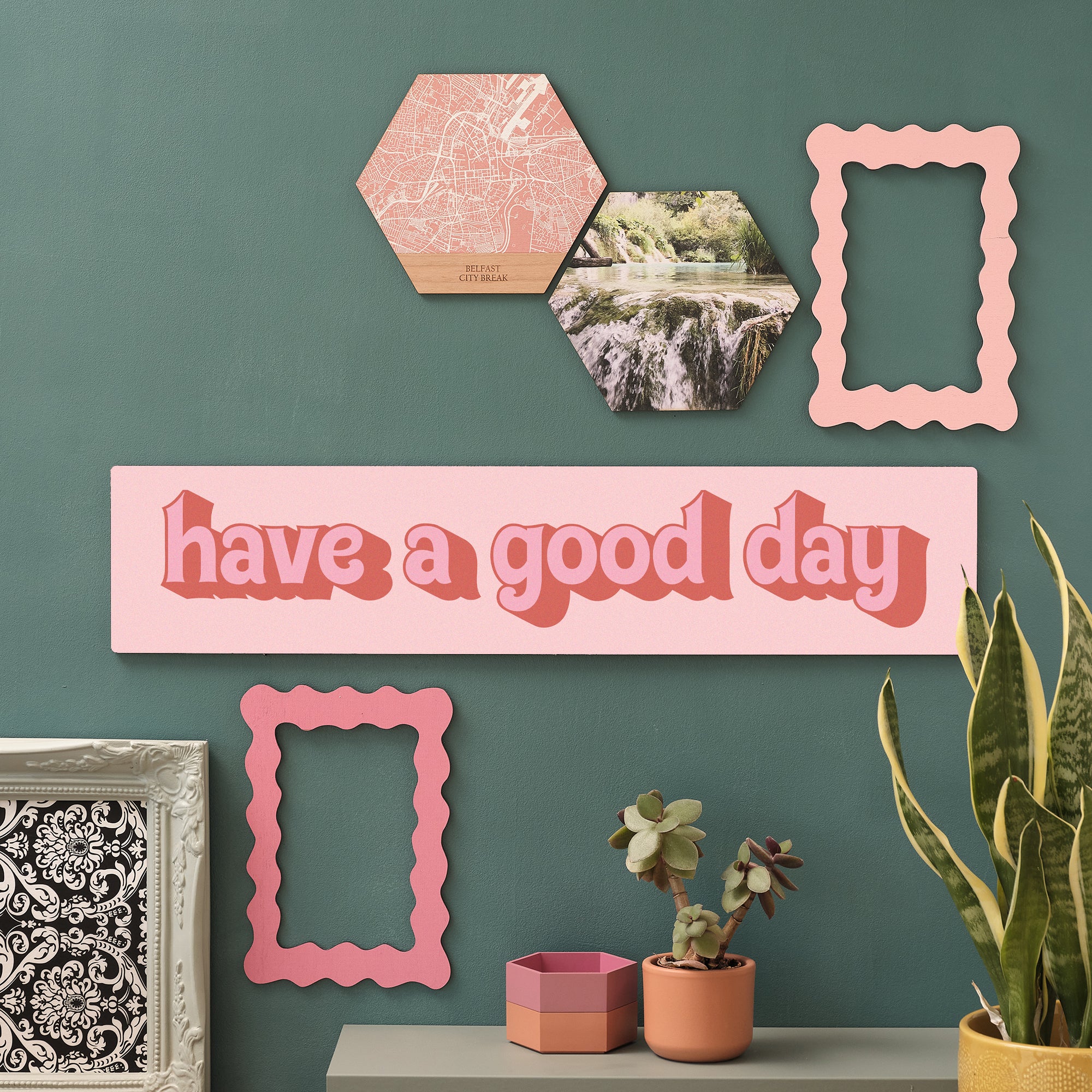 “Have a Good Day” in pinks wooden sign on green gallery wall with plants and photo hexagons