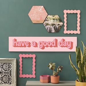 “Have a Good Day” in pinks wooden sign on green gallery wall with plants and photo hexagons