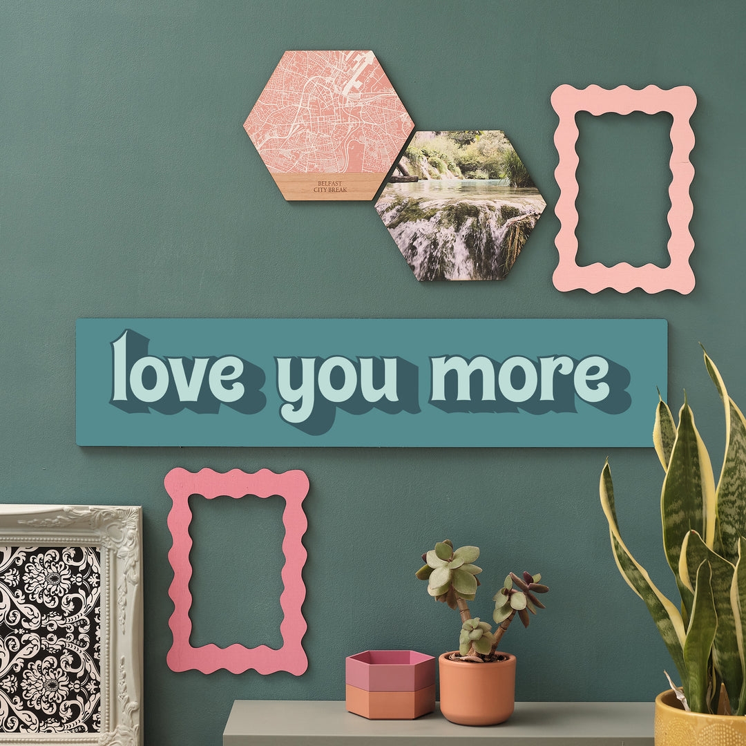 Wooden “Love You More” sign on green wall with gallery of hexagon art and plants – perfect hallway decor
