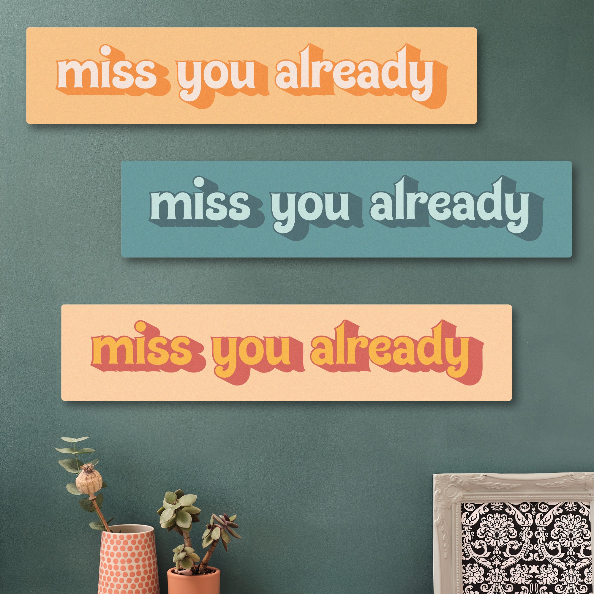Quirky cherry wood sign with the message “Miss You Already” surrounded by funky wall art and home decor. colourways feature yellows and teals.