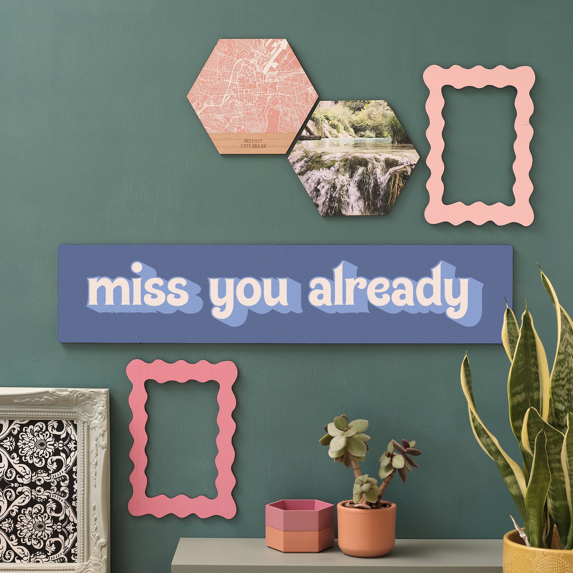 Quirky cherry wood sign with the message “Miss You Already” surrounded by funky wall art and home decor. colourways feature yellows and teals.