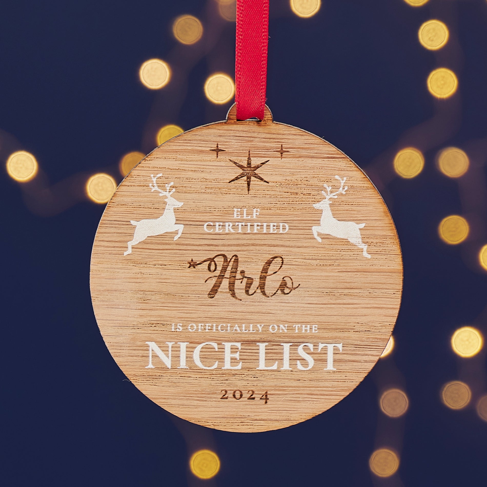 A round wooden Christmas ornament with the name "Arlo" engraved on it, along with the message "Elf Certified - Is Officially on the Nice List 2024" and two leaping reindeer.

