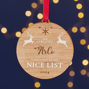 A round wooden Christmas ornament with the name "Arlo" engraved on it, along with the message "Elf Certified - Is Officially on the Nice List 2024" and two leaping reindeer.

