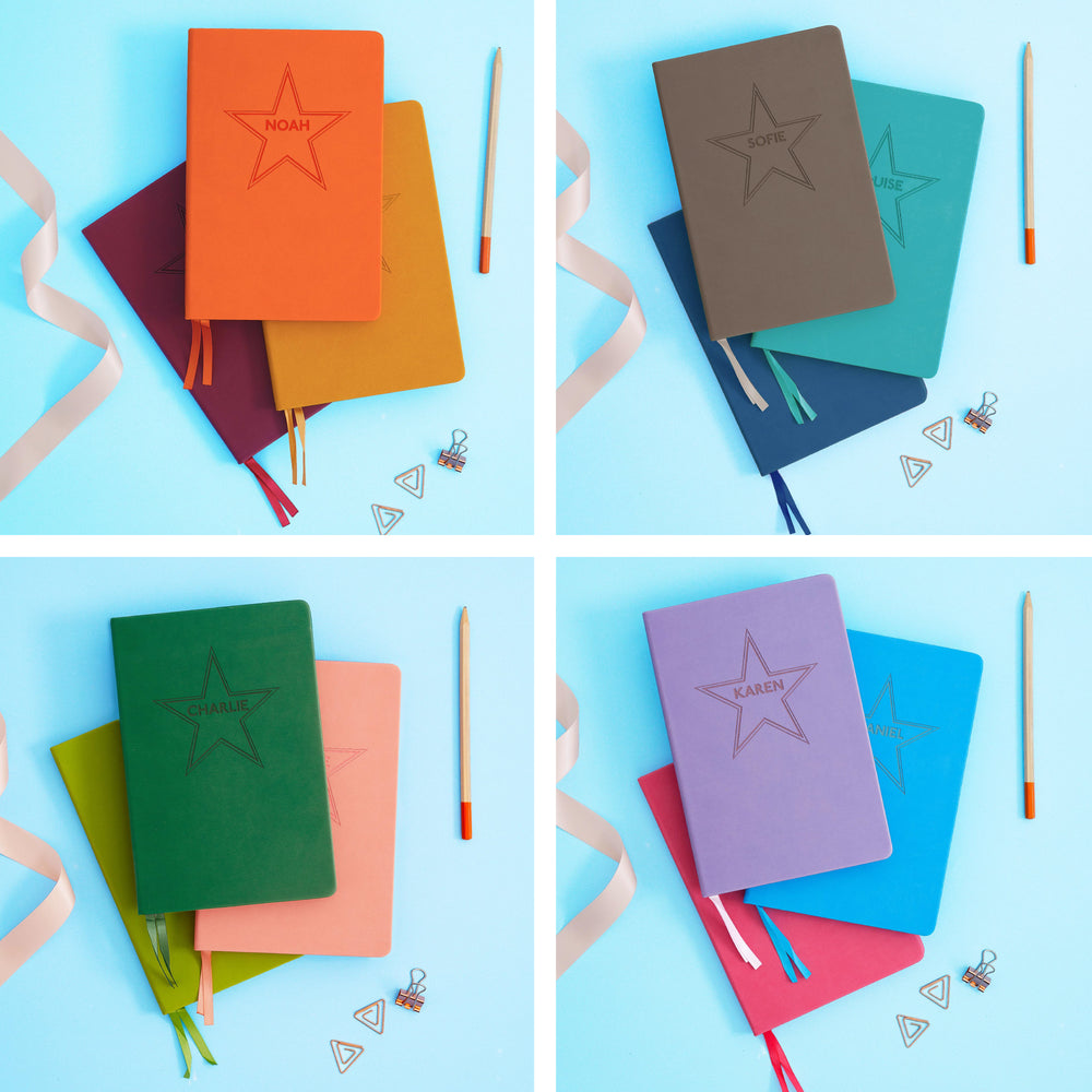 The image shows examples of personalised engraved text on all 12 colours of notebook. The books are stacked in threes and are surround by various pieces of stationery.