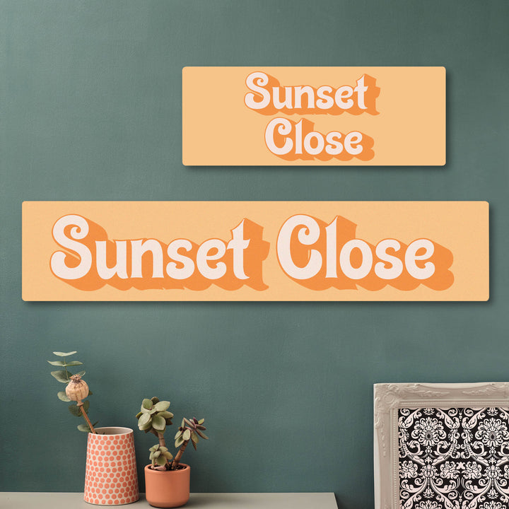 Two wooden custom printed sustainable cherry veener signs with 'Sunset Close' text on a green wall. New home gift for couples.