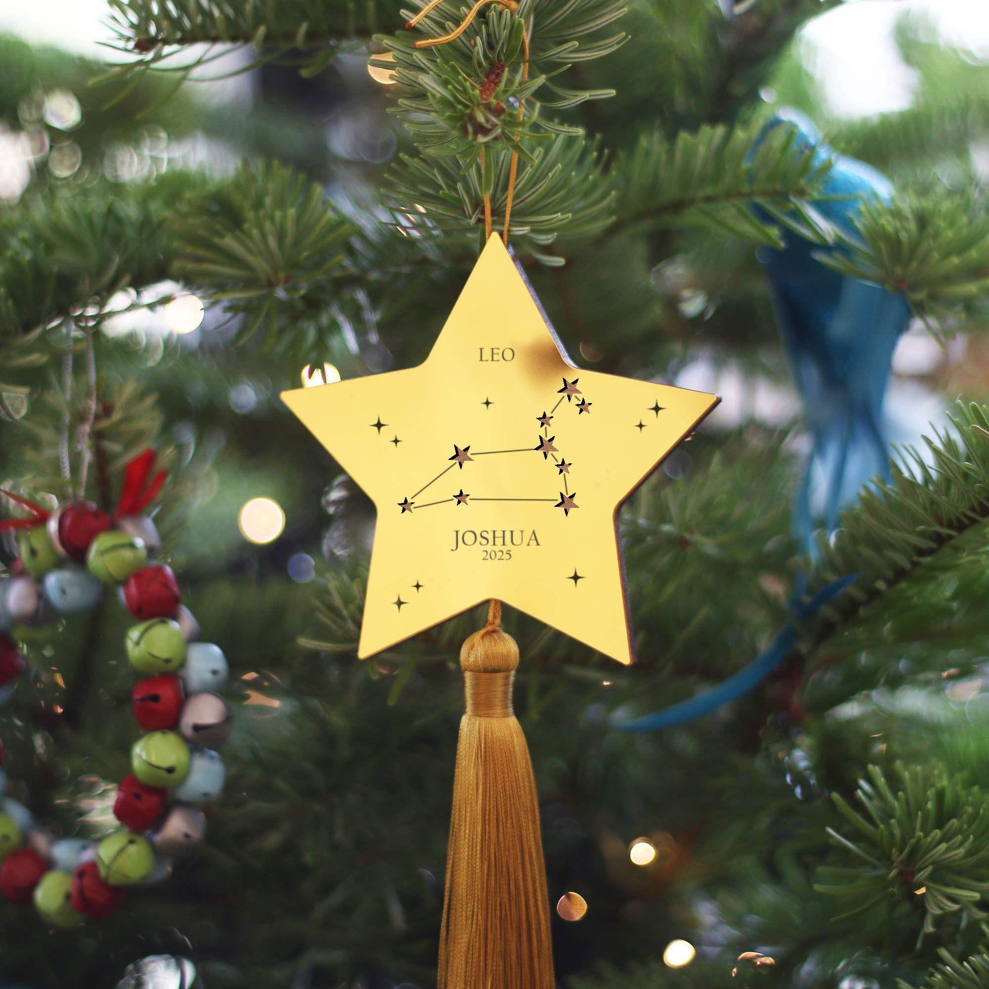 Gold star-shaped ornament with tassel against a dark blue background with bokeh lights