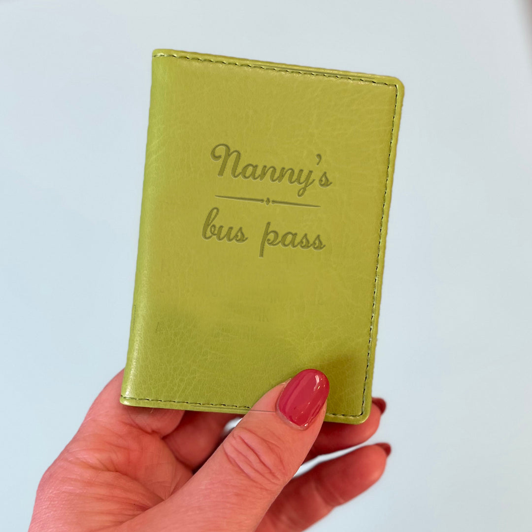 A womans hand holds a green custom ID holder/bus pass leather holder. The front of the slim style wallet has been personalised with the words Joanne's bus pass.