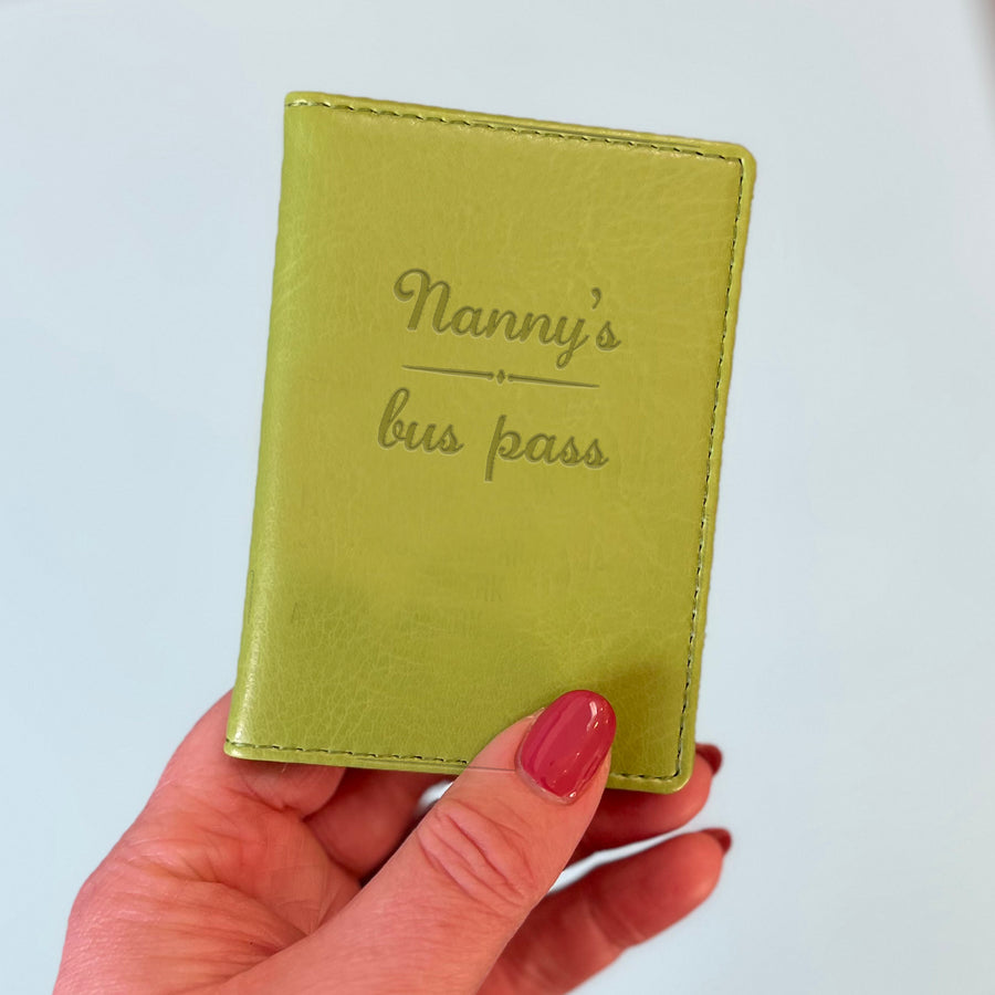 A womans hand holds a green custom ID holder/bus pass leather holder. The front of the slim style wallet has been personalised with the words Joanne's bus pass.