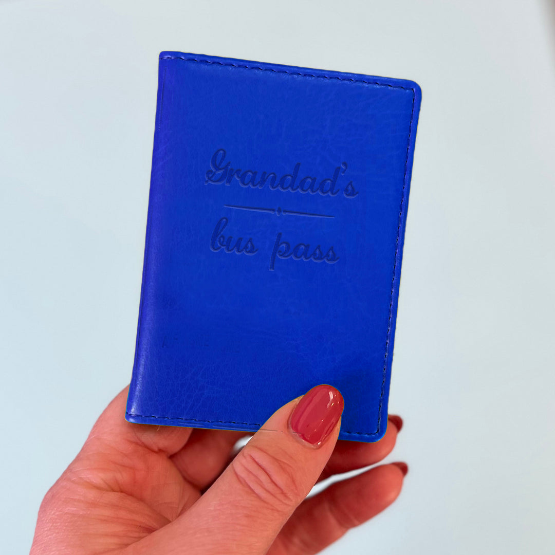 A womans hand holds a royal blue custom ID holder/bus pass leather holder. The front of the slim style wallet has been personalised with the words Grandad's bus pass.