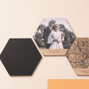 Three wooden photo tiles showing a solid black colour, a wedding photo with personalised tex, and a black line map. Hung on a pink wall.