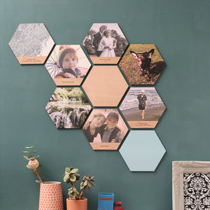 A collage of hexagonal wooden tiles featuring photos, maps, and solid colours. Some tiles also have personalised engraved text.  Mounted on a green wall.