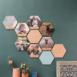 A collage of hexagonal wooden tiles featuring photos, maps, and solid colours. Some tiles also have personalised engraved text.  Mounted on a green wall.