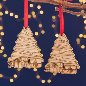 Two personalized wooden Christmas tree ornaments with engraved names, hanging from red ribbons against a background of warm fairy lights.