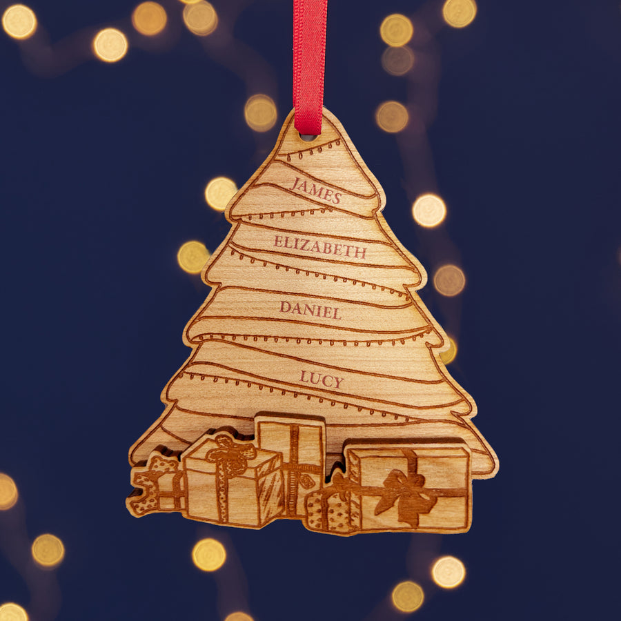 A personalized wooden Christmas tree ornaments with engraved names, hanging from red ribbons against a background of warm fairy lights.