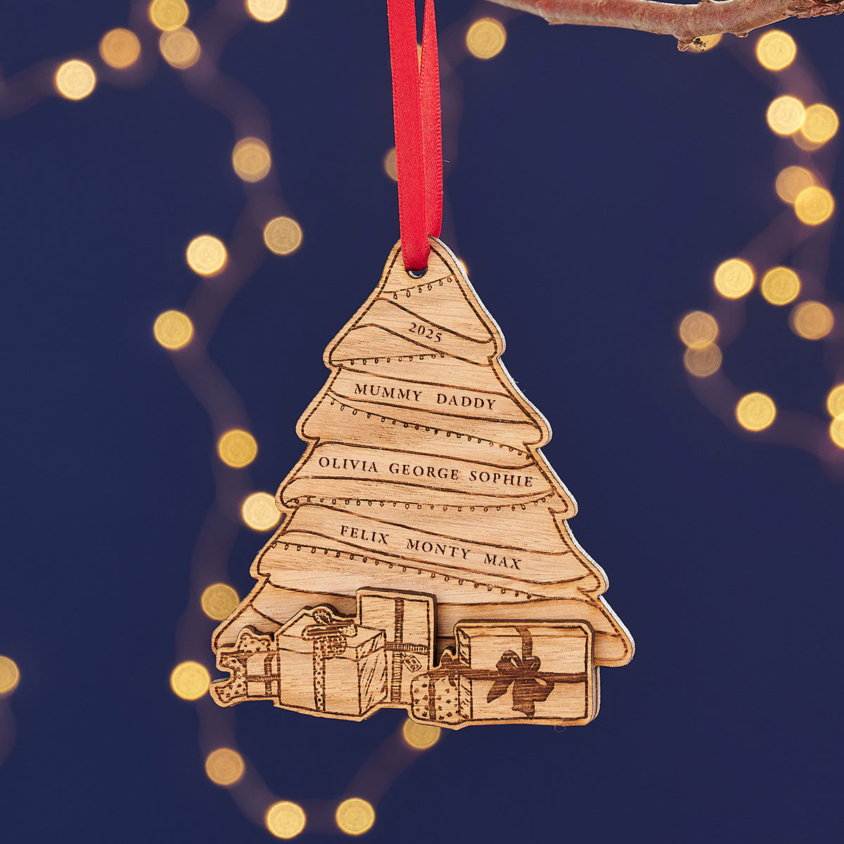 A personalized wooden Christmas tree ornaments with engraved names, hanging from red ribbons against a background of warm fairy lights.