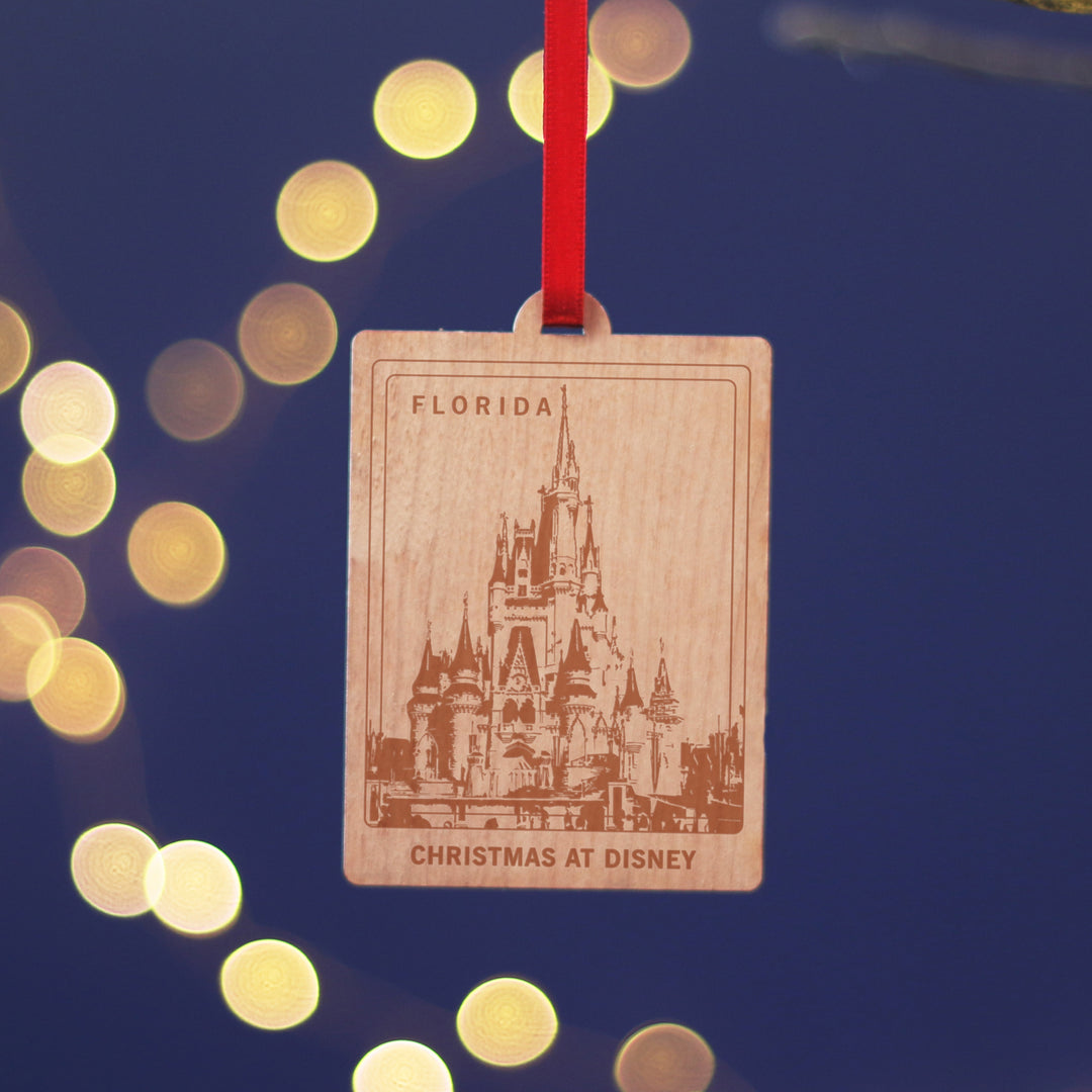 Florida travel memory anniversary gift, commemorate your Christmas memories, with this sustainable wood cherry veneered ornament with The Disney Castle. Hanging against a blue background. Personalise the location and text for a perfect letterbox friendly gift for travellers.