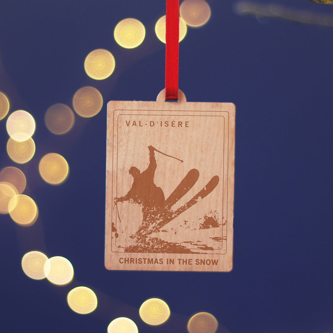 Val-D'Isere travel memory anniversary gift, commemorate your Christmas memories, with this sustainable wood cherry veneered ornament with ta skier. Hanging against a blue background. Personalise the location and text for a perfect letterbox friendly gift for travellers.