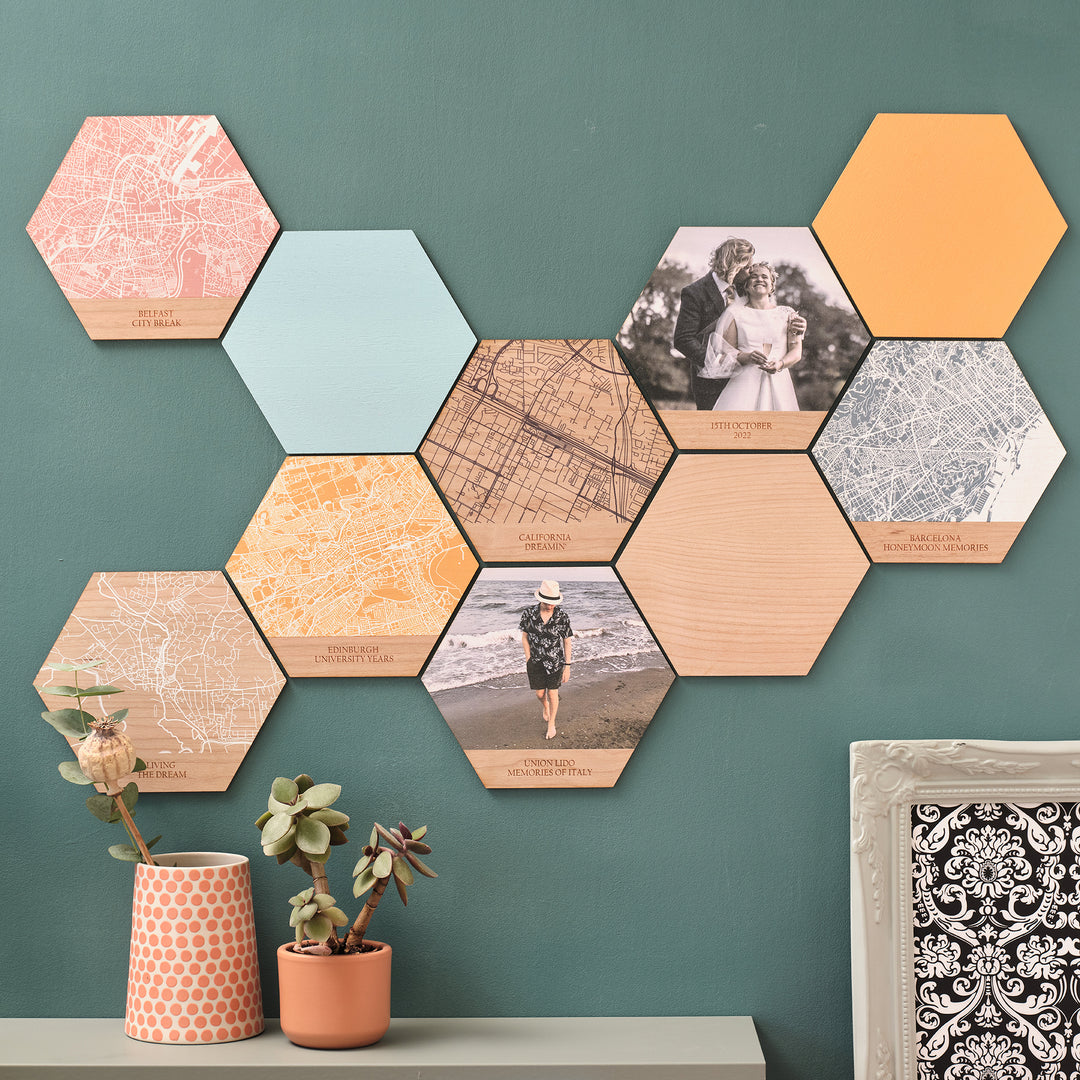 An assortment of printed wooden hexagonal wall arts tessellated on a green wall with potted plants in front. Vibrant colours for anyone's home decor desires, upload your own photo, map location and text for a personalised unique centrepiece.