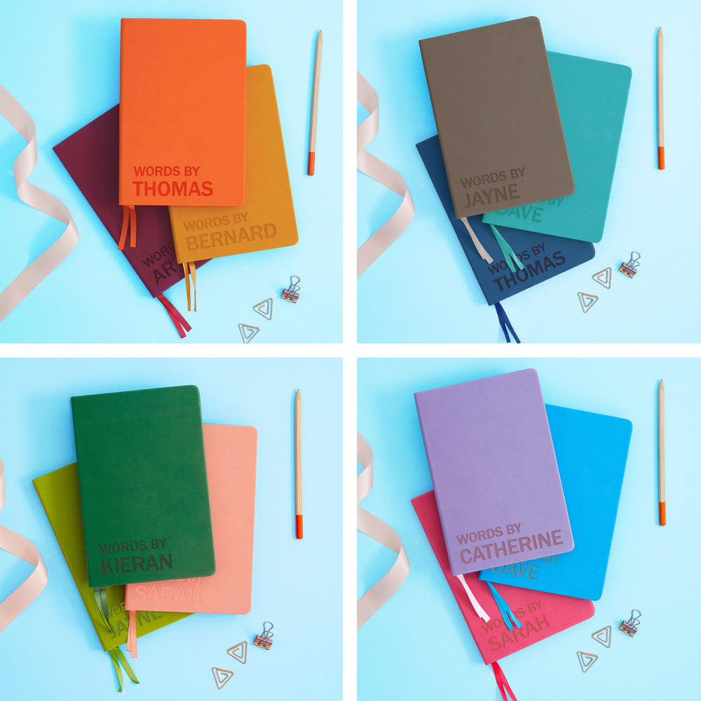 The image shows examples of personalised engraved text on all 12 colours of notebook. The books are stacked in threes and are surround by various pieces of stationery.