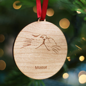 Cute cat nose engraved wooden bauble, eco Christmas gift for pet owners. Shown hanging on a Christmas tree by a red satin ribbon.