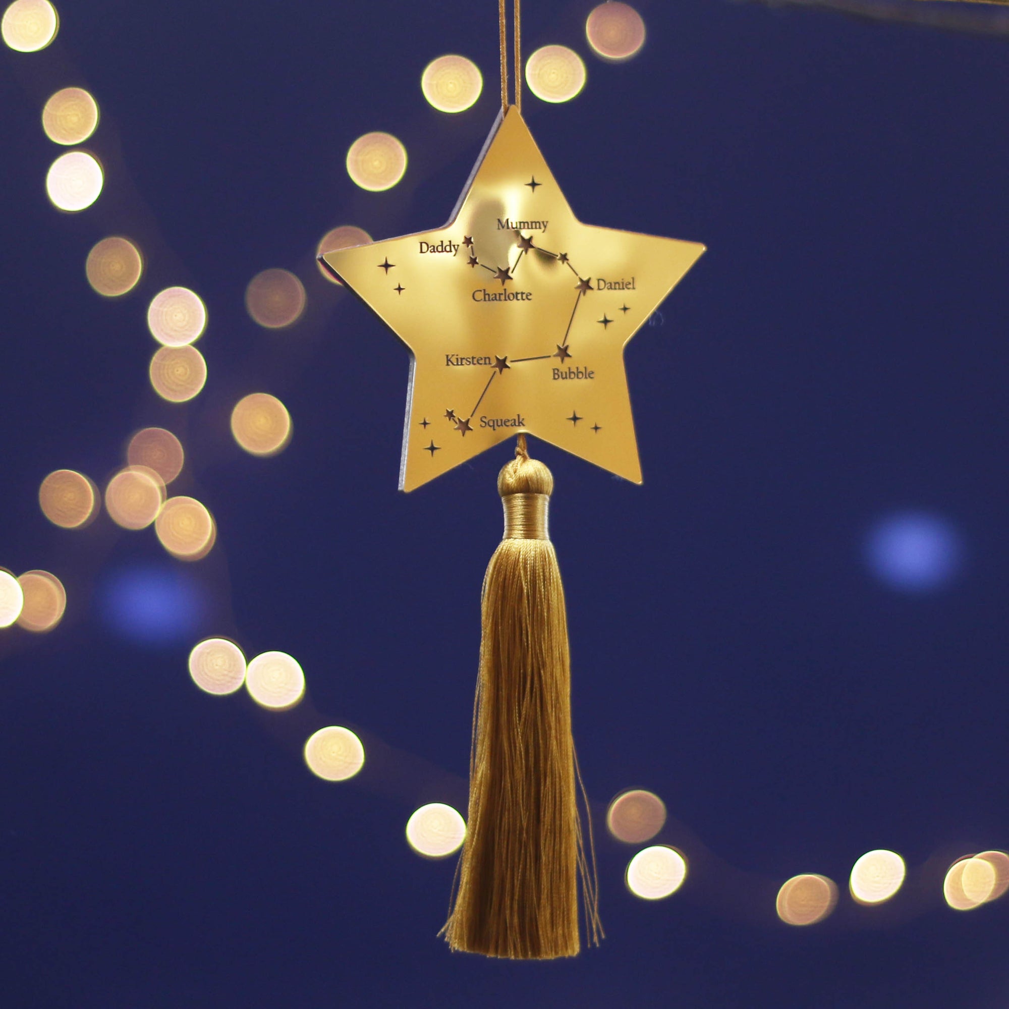 Gold star-shaped ornament with tassel against a dark blue background with blurred lights