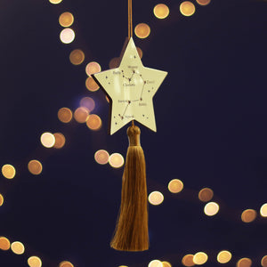 Decorative star ornament with tassel against a dark background with bokeh lights